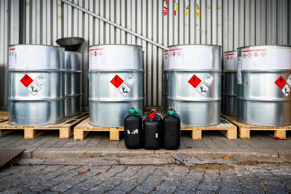 Hazard-labelled chemical-waste drums and containers in industrial storage.