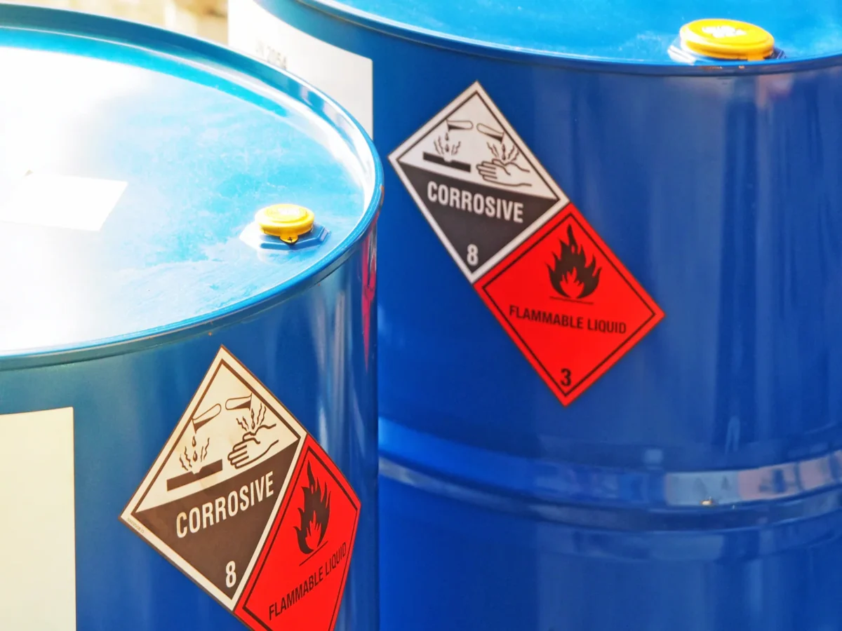 Blue chemical drums carrying corrosive and flammable hazard labels.